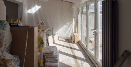Home renovation in progress with drywall work, construction materials, and large sliding glass doors bringing natural light into a Michigan home