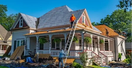 Home undergoing roof repair and restoration after damage with workers replacing shingles