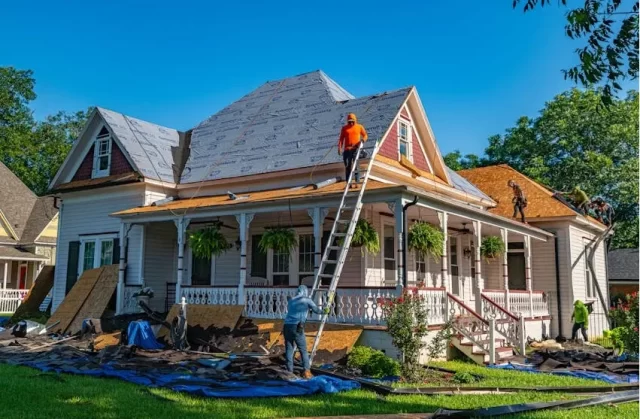 Home undergoing roof repair and restoration after damage with workers replacing shingles